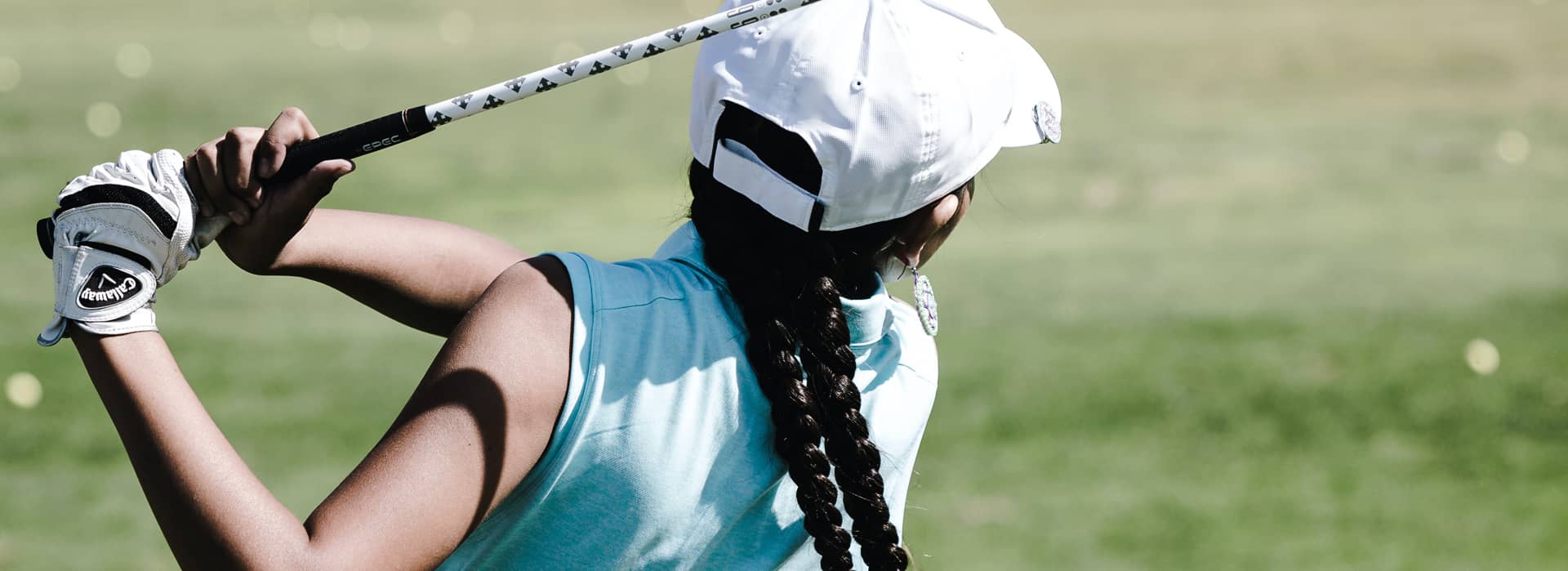 a photo of a woman with a blue shirt and white hat after just having taken a golf swing